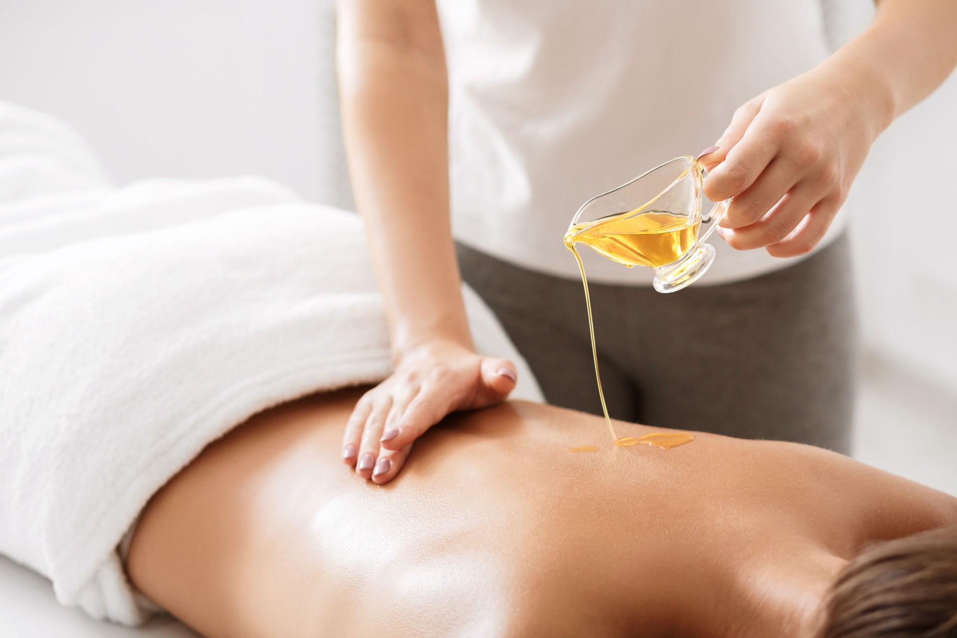 Masseur pouring aroma oil on female back