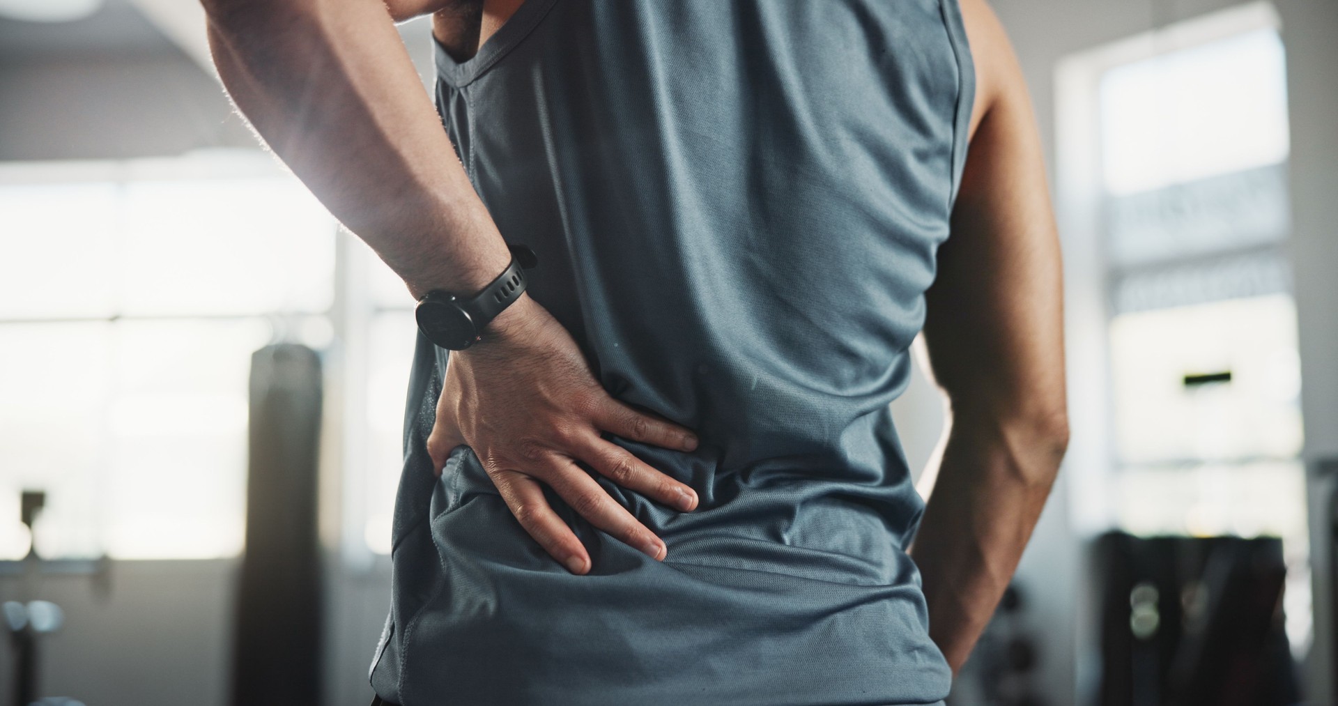 Man, hands and back pain with injury at gym for muscle tension, workout accident or sprain. Closeup, male person or athlete with sore spine, pinch nerve or ache for joint inflammation at health club