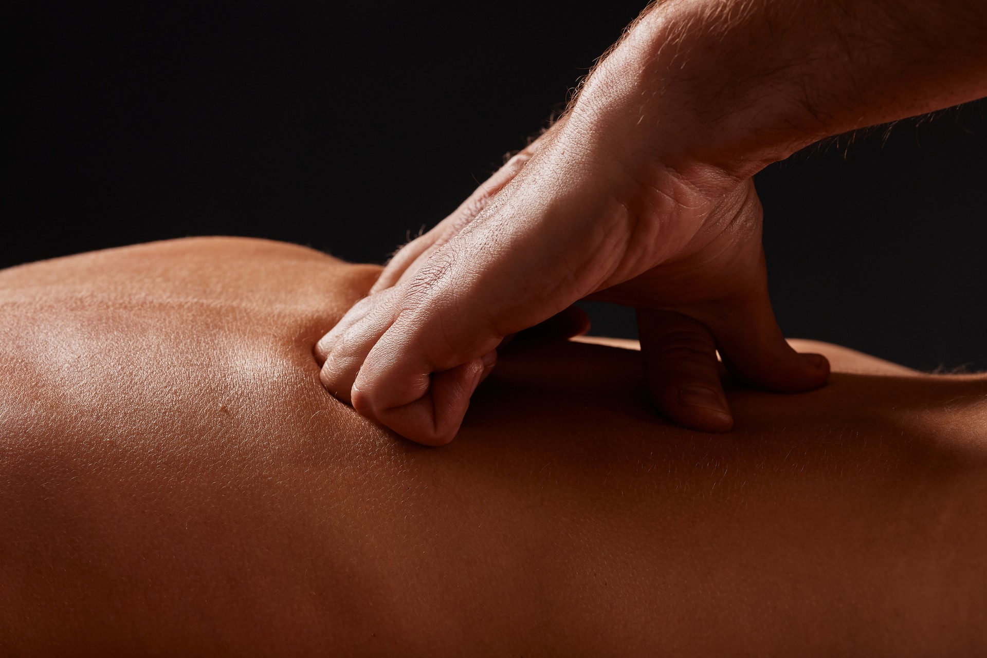 handsome male masseur giving massage to girl on black background, concept of therapeutic relaxing massage